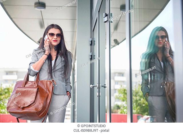 Businesswoman walking beside office building, using smartphone