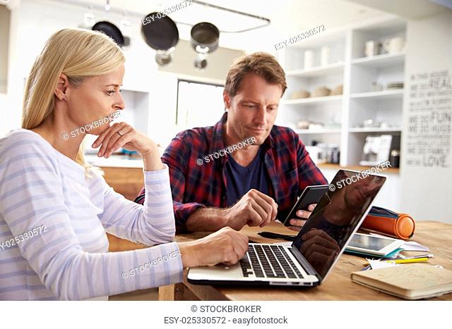 Stressed couple sitting in their kitchen using computers