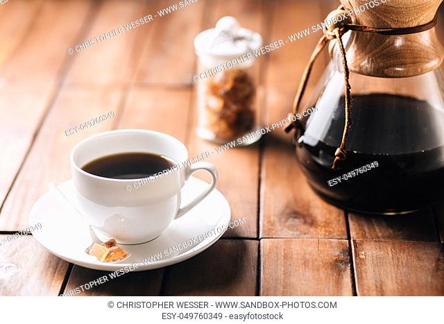 A tabletop scene with coffee, more coffee running through a coffee maker and some rock candy on a wooden table