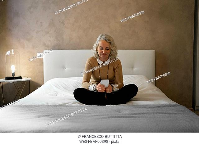 Portrait of mature businesswoman sitting on bed using mobile phone
