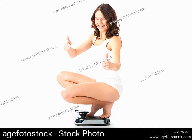 Diet and weight, young woman sitting on her haunches on a scale, she is happy about the success