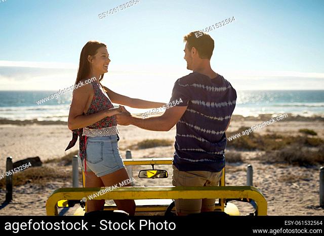 Happy caucasian couple in beach buggy by the sea holding hands