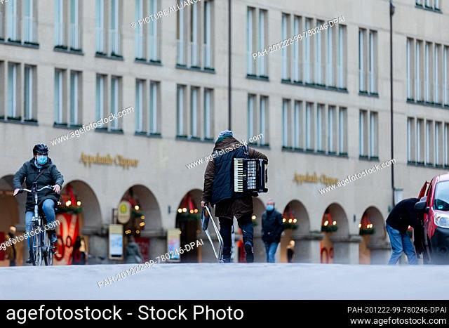21 December 2020, North Rhine-Westphalia, Münster: A man with an accordion walks across Prinzipalmarkt. Photo: Rolf Vennenbernd/dpa