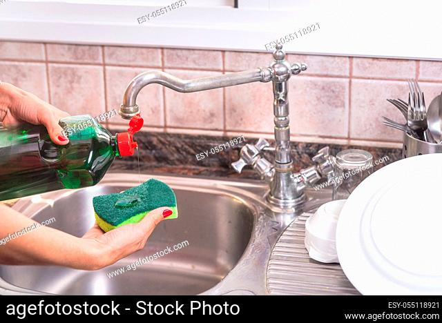 woman with red manicure putting detergent in the scourer, to wash the dishes