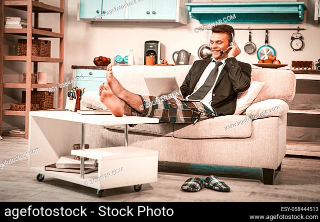 Cheerful Businessman Works From Home, Caucasian Man In Headphones Surfing Net While Putting Legs On Coffee Table, Freelancer In Business Top And Casual Pants...