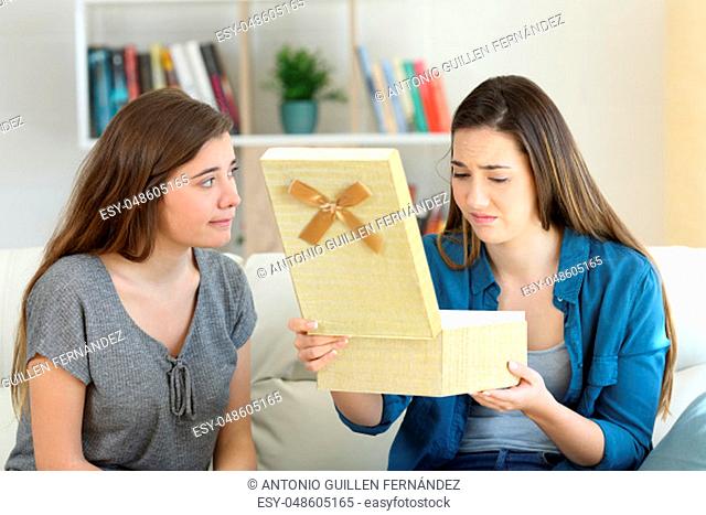 Disappointed girl opening a gift beside her friend sitting on a couch in the living room at home