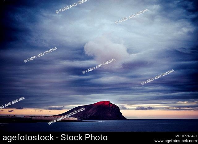 beautiful landscape tenerife montana roja during a blue sunset with red light on the top of the mounts. ocean and clouds for timeless beauty