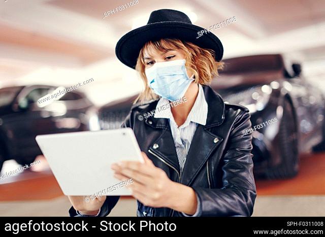 Young urban woman in mask and hat using tablet