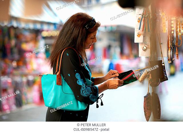 Mature female tourist looking beaded purse on market stall, Sharjah, United Arab Emirates
