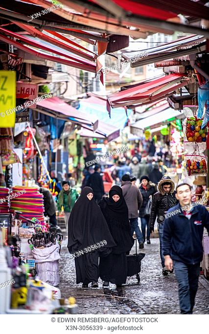 Two women wearing chadors walk along narrow street under awnings in outdoor market , Istanbul, Turkey