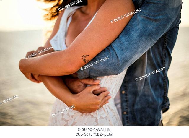 Romantic couple hugging on coast, mid section, Santa Teresa Gallura, Sardinia, Italy