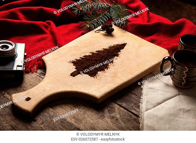 The two cups of coffee on wooden background and christmas tree made of ground coffee on a cutting board