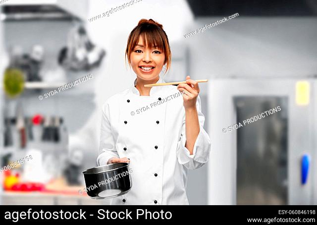 female chef with saucepan tasting food on kitchen