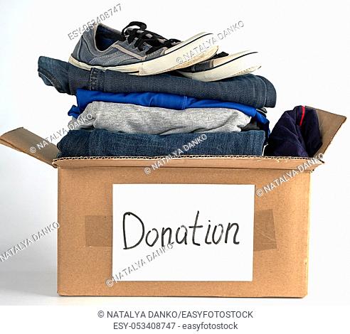 folded clothes and shoes in a brown paper box with the inscription donation on a white background, the concept of helping people in need