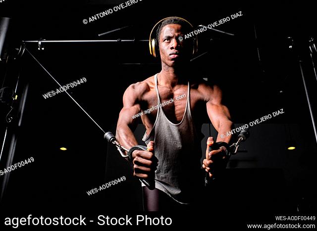 Determined young man listening music through headphones while practicing suspension exercise at gym