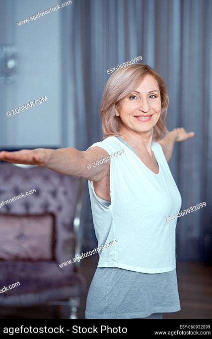 Smiling Woman Stretches Her Arms To The Sides. Happy Middle-Aged Woman Does Standing Yoga Poses. Healthy Lifestyle