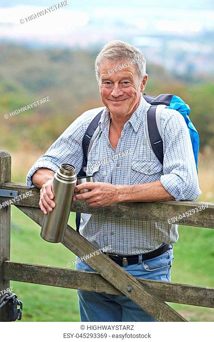 Portrait Of Senior Man On Hike In Countryside Resting By Gate And Having Hot Drink