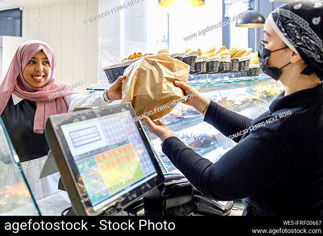 Smiling woman wearing hijab buying food from owner at bakery