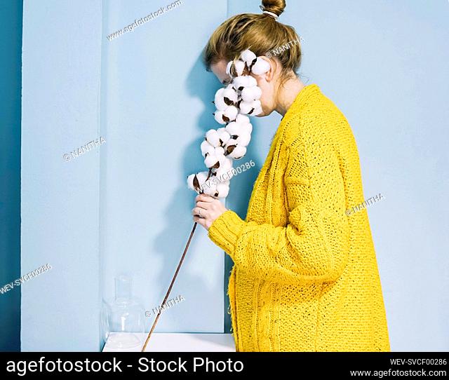 Woman covering face with cotton plant at home