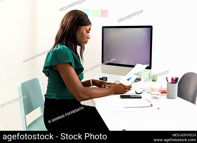 Businesswoman analyzing graph paper while sitting by desk at office
