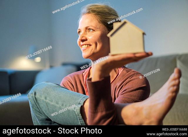 Happy mature woman holding house model exercising at home