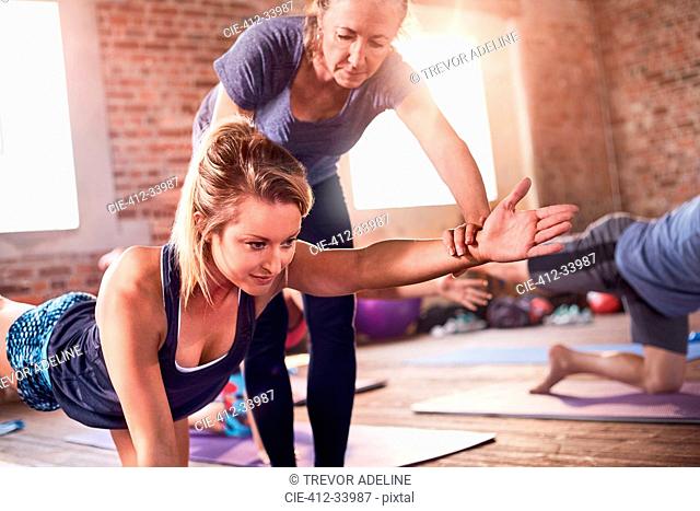 Fitness instructor helping young woman practicing bird dog plank in exercise class gym studio