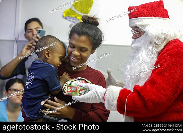 15 December 2023, Venezuela, Caracas: Children from the poor neighborhood of Petare receive presents from a man dressed as Santa Claus during the gift handover...