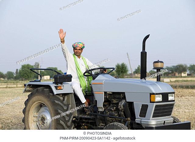 Farmer ploughing a field with a tractor and waving his hand