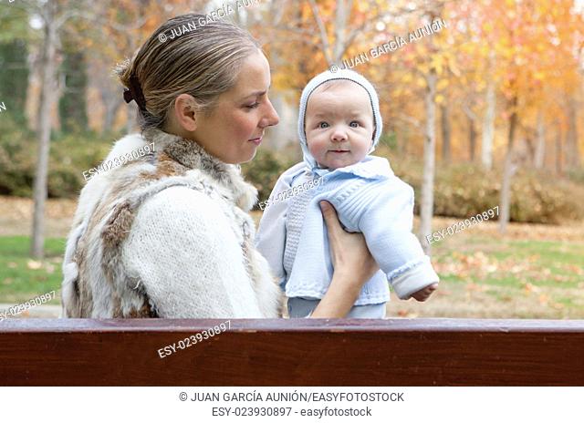 Happy mother playing with his baby in the park on the bench on winter season
