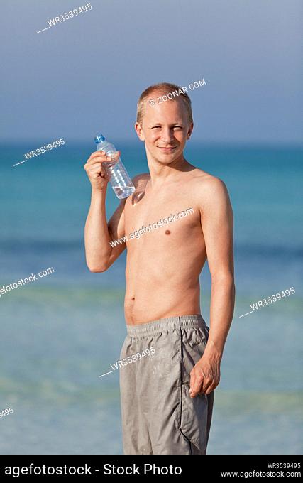 Junger Mann Junge trinkt erfrischendes Wasser aus einer Flasche am Strand am Meer im Sommer Urlaub