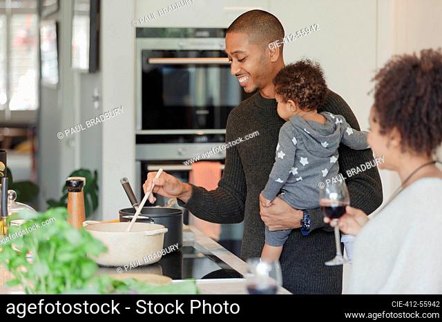 Happy couple with baby daughter cooking dinner in kitchen