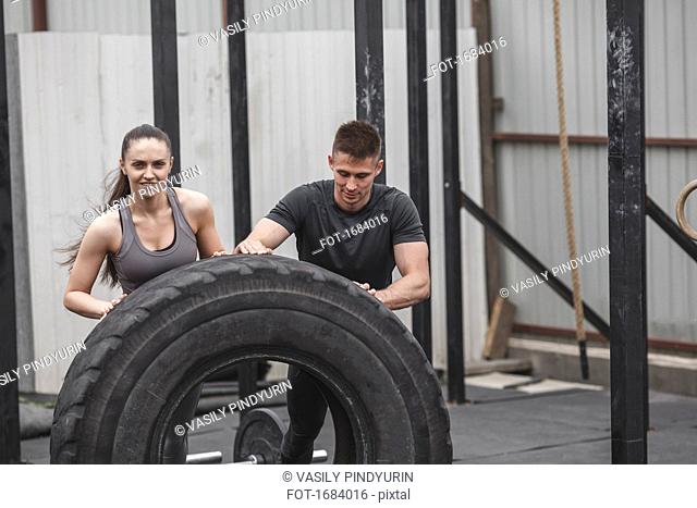 Male instructor assisting female athlete in flipping tire during crossfit training