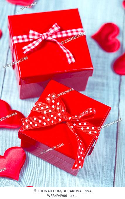 Gift box and pink roses in a cup and red beads on wooden background. Vintage color toning