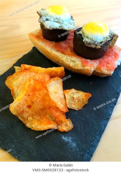 Spanish tapa made of morcilla and quail eggs on bread with tomato and chips. Spain