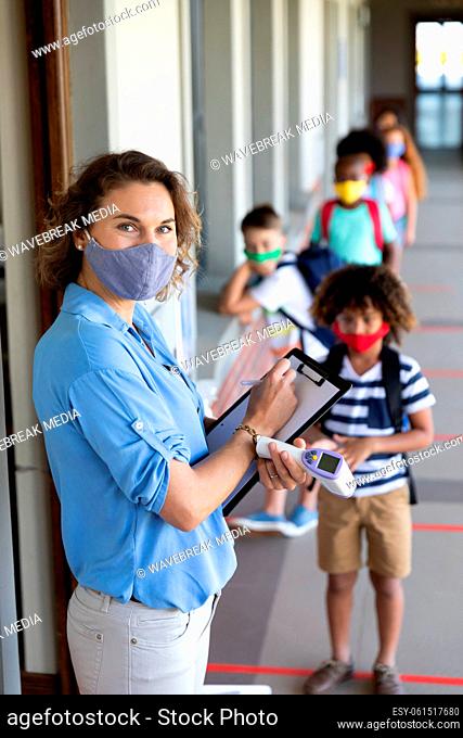 Portrait of female teacher wearing face mask with clipboard and temperature gun