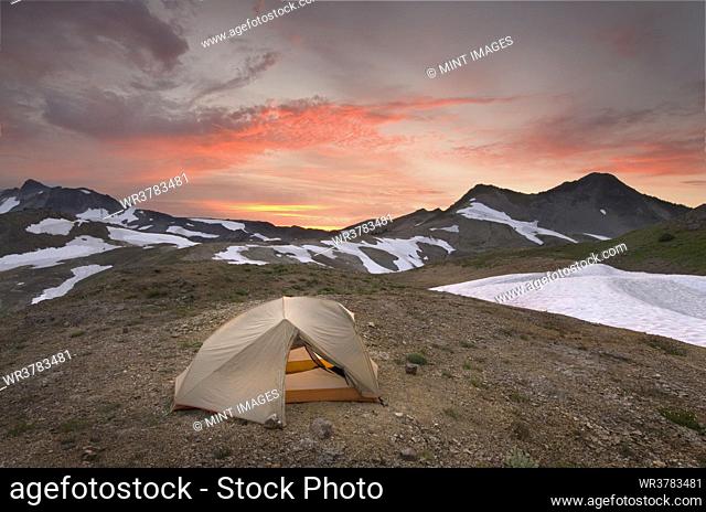 A small tent pitched on a screen slope just below the snowline, at sunset in the Mount Baker wilderness
