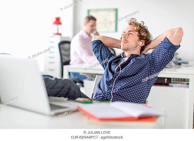 Young office worker reclining at desk with hands behind head