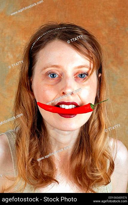 Young woman with spicy red hot chili pepper inside her mouth