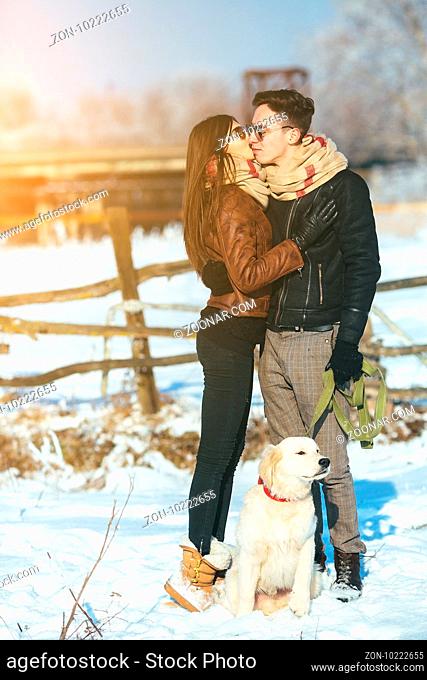 Cute young hipster couple posing in winter park with their dog on a bright day