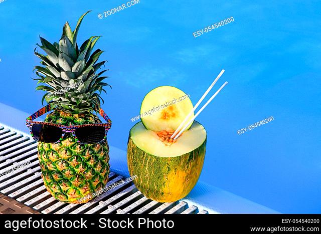 Pineapple wearing sunglasses and melon at blue swimming pool