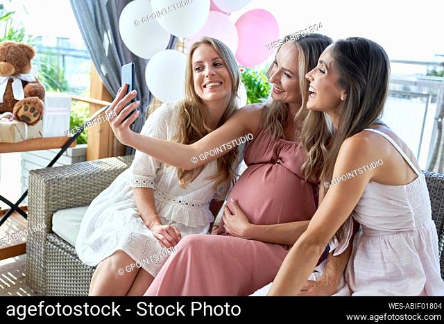 Happy pregnant woman taking selfie with friends through smart phone at baby shower