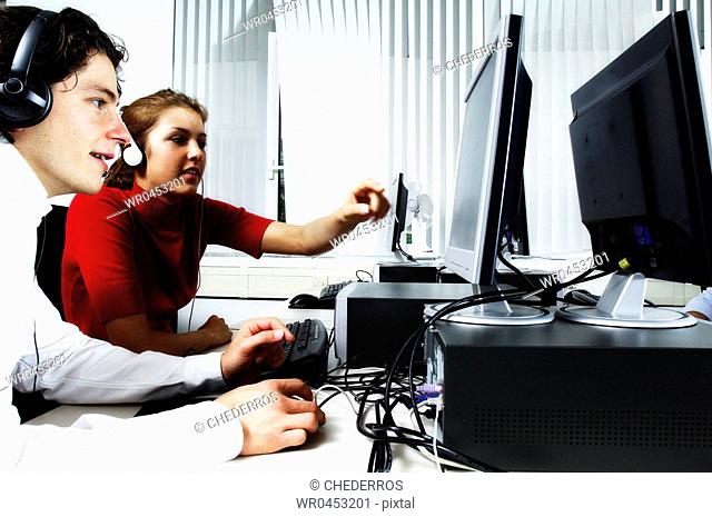 Teenage girl pointing to a computer with a teenage boy sitting beside her wearing a headset