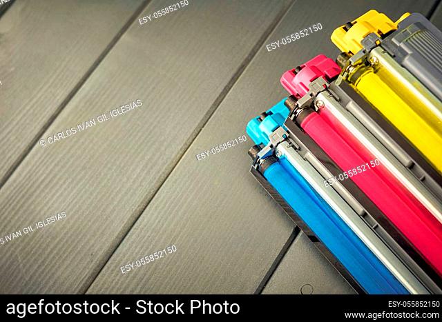 Cartuchos de toner amarillo, cyan y magenta para sustitución en una impresora de color sobre fondo de madera