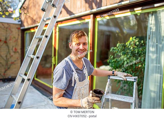 Portrait confident male painter with ladder painting home exterior
