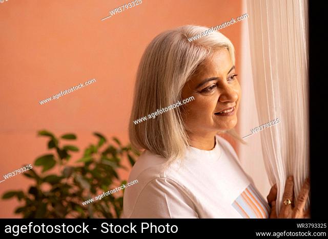 Close-up portrait of old woman looking out of window