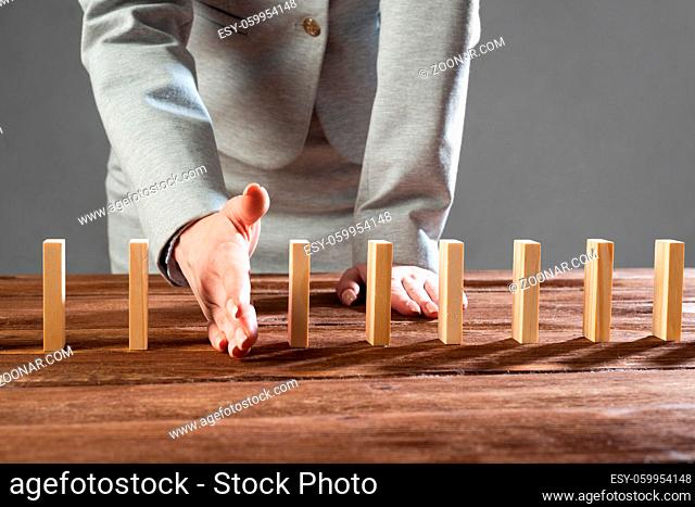 Businesswoman interrupting domino effect by stop falling wooden dominoes. Operative business solution, strategy and successful intervention
