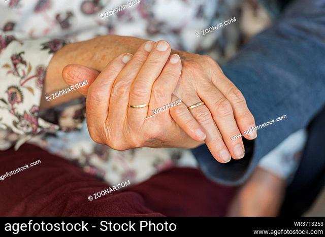 Close-up of holding hands of an 80 year old couple with wedding rings. Nahaufnahme einander haltender Hände eines 80-jähringen Ehepaars mit Eheringen