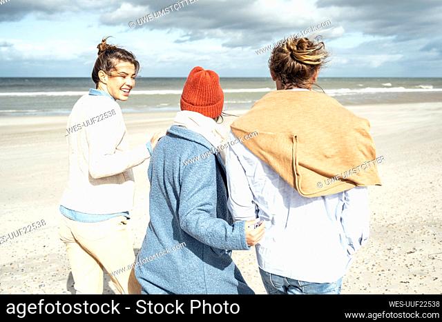 Group of friends walking together along sandy coastal beach
