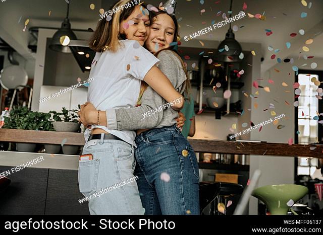 Loving teenage friends embracing while standing in birthday party at home