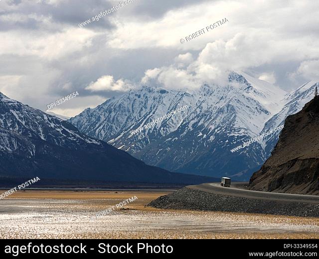 Transport truck driving the Alaska Highway along side the dried up portion of Kluane Lake with huge mountains in the distance